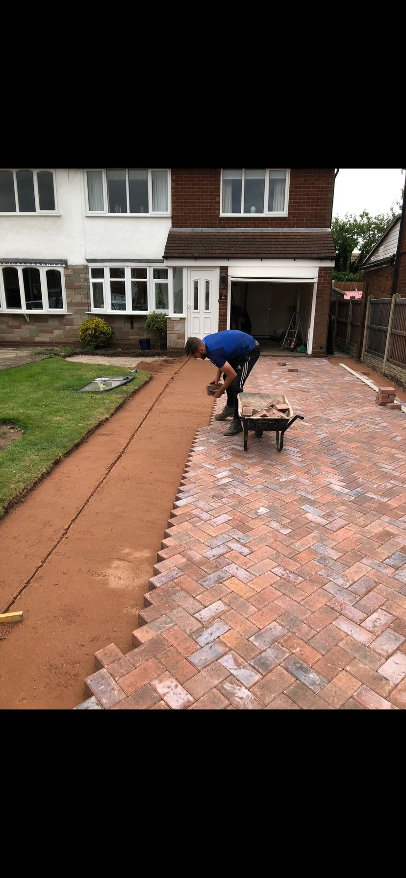 Person laying bricks on a newly paved driveway in front of a house.