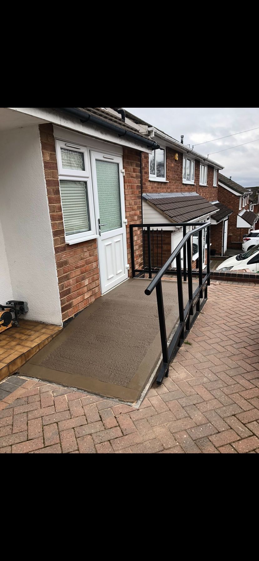 Newly constructed wheelchair ramp with black railings leading to a white door of a brick house.