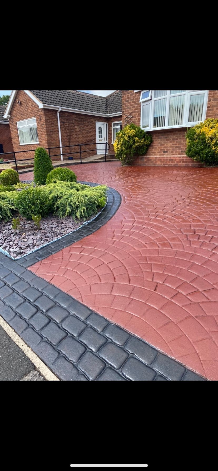 Well-maintained brick house with a decorative circular garden and patterned red brick driveway.