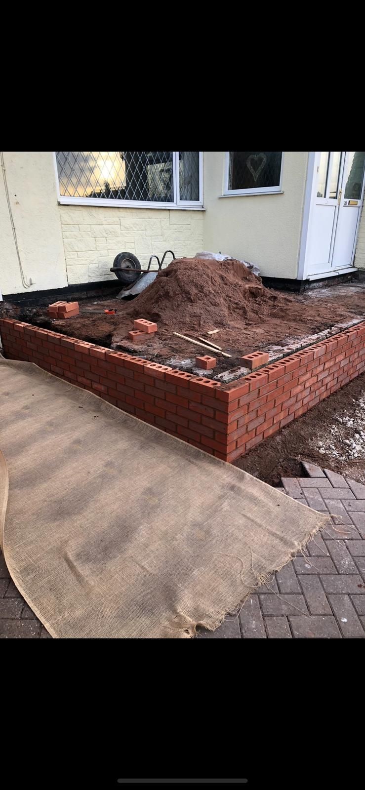 Brick foundation with soil and construction materials next to a house window and door.