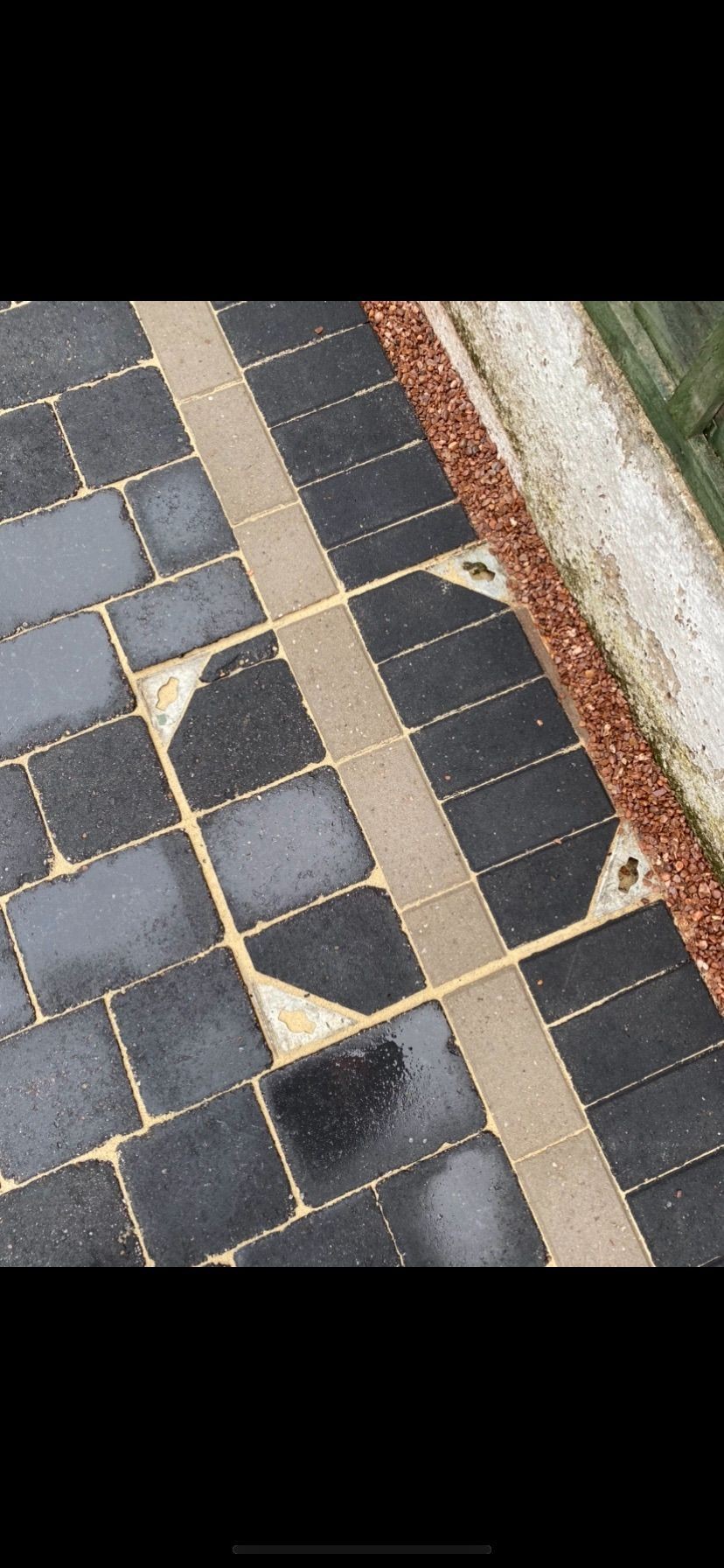 Wet black paving stones with a lighter border and small gravel section next to a wall.