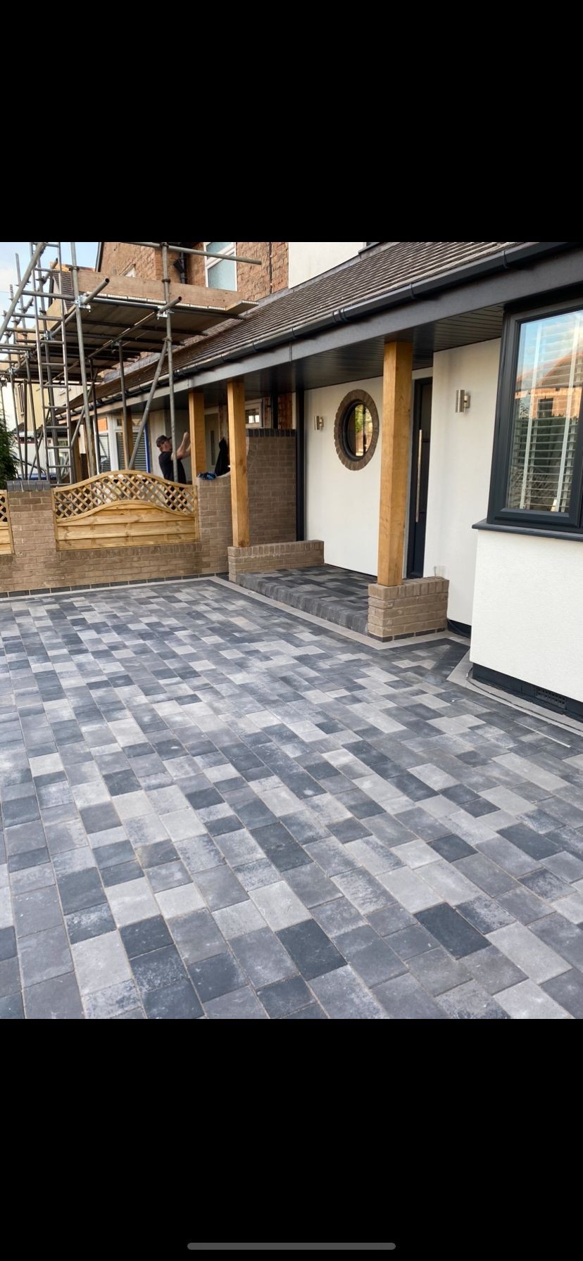 Resurfaced driveway with gray paving stones in front of a house under construction with scaffolding.